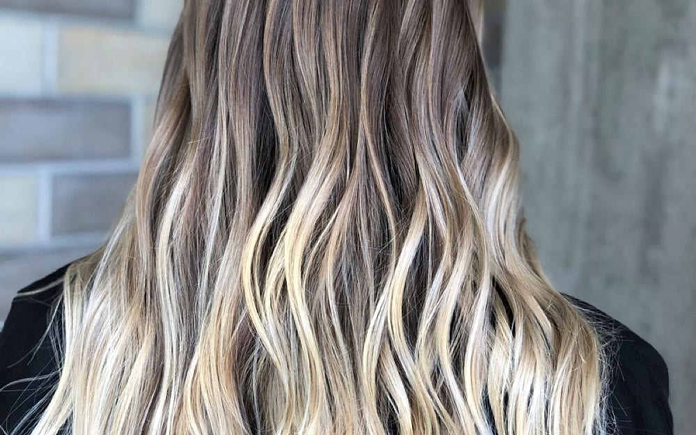 Long wavy hair with soft, hand-painted blonde balayage, seen from behind